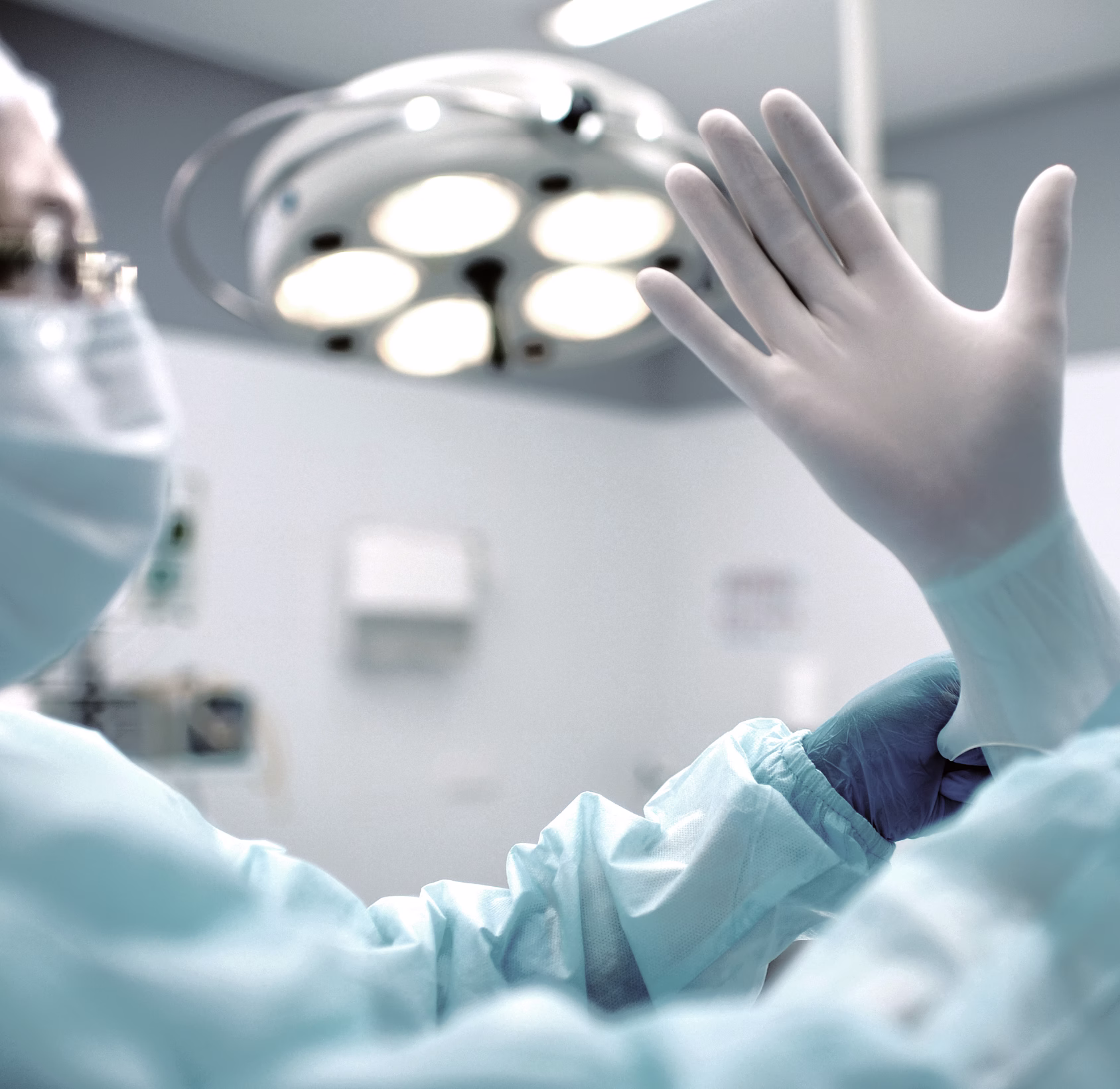 A medical professional wearing a surgical mask and gloves is preparing for a procedure, with a focus on their hand as they don a surgical glove.