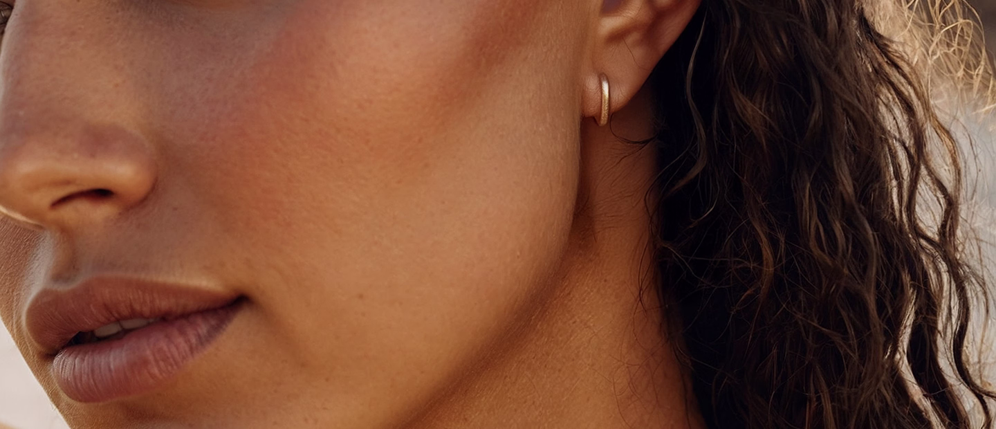 A close-up image of a woman's face featuring curly hair, with a subtle smile and wearing a small, simple hoop earring.