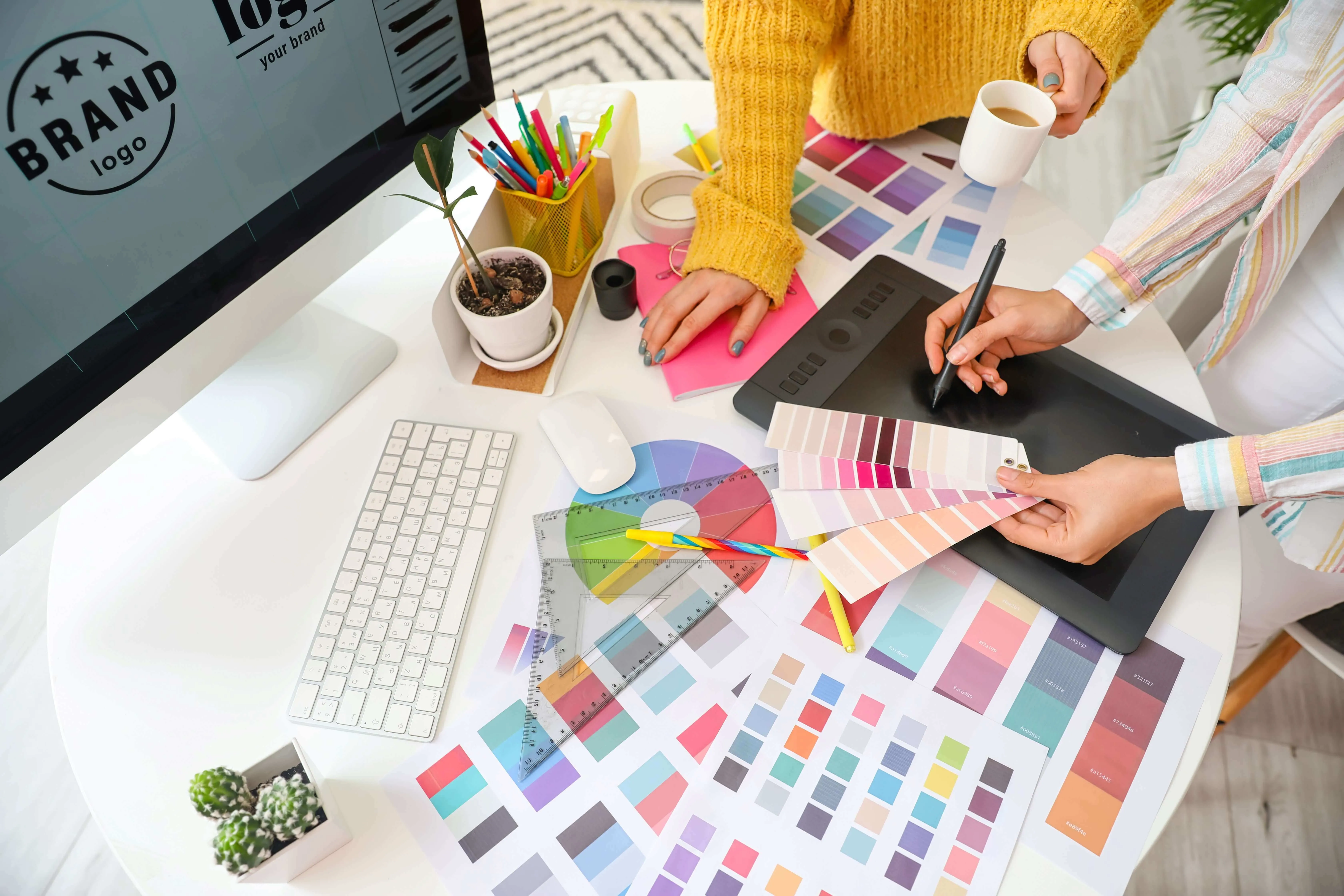 Designer arbeiten gemeinsam mit Farbfächern und Grafiktablett an einem Branding-Konzept am Schreibtisch