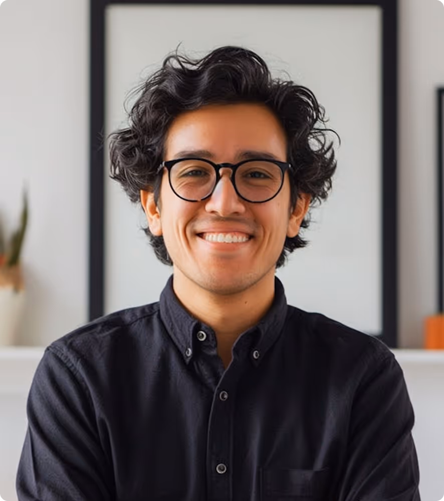 Smiling young man with curly dark hair and glasses wearing a black button-up shirt.