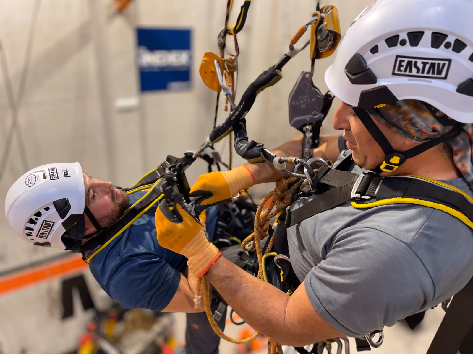 Varias personas con cascos y arneses de seguridad en un gimnasio de entrenamiento de trabajos en altura con estructuras metálicas y cuerdas.