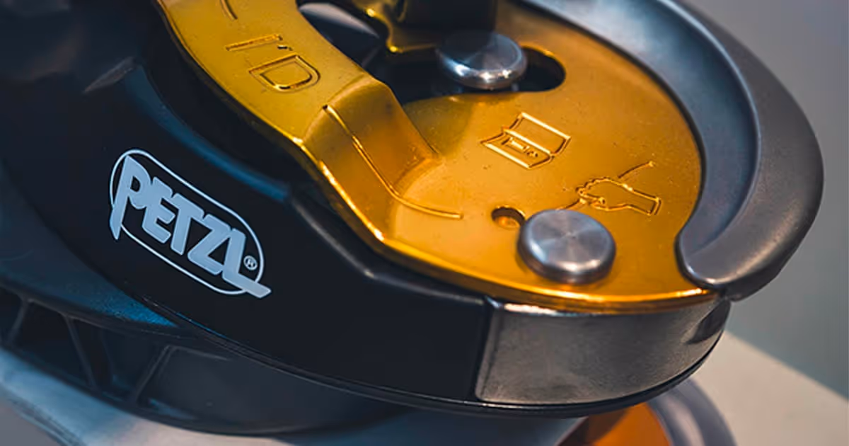 Dispositivo de descenso Petzl con placas metálicas doradas y negro, usado para trabajos en altura.