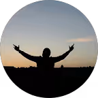 Silueta de una persona con los brazos levantados al atardecer con cielo despejado.