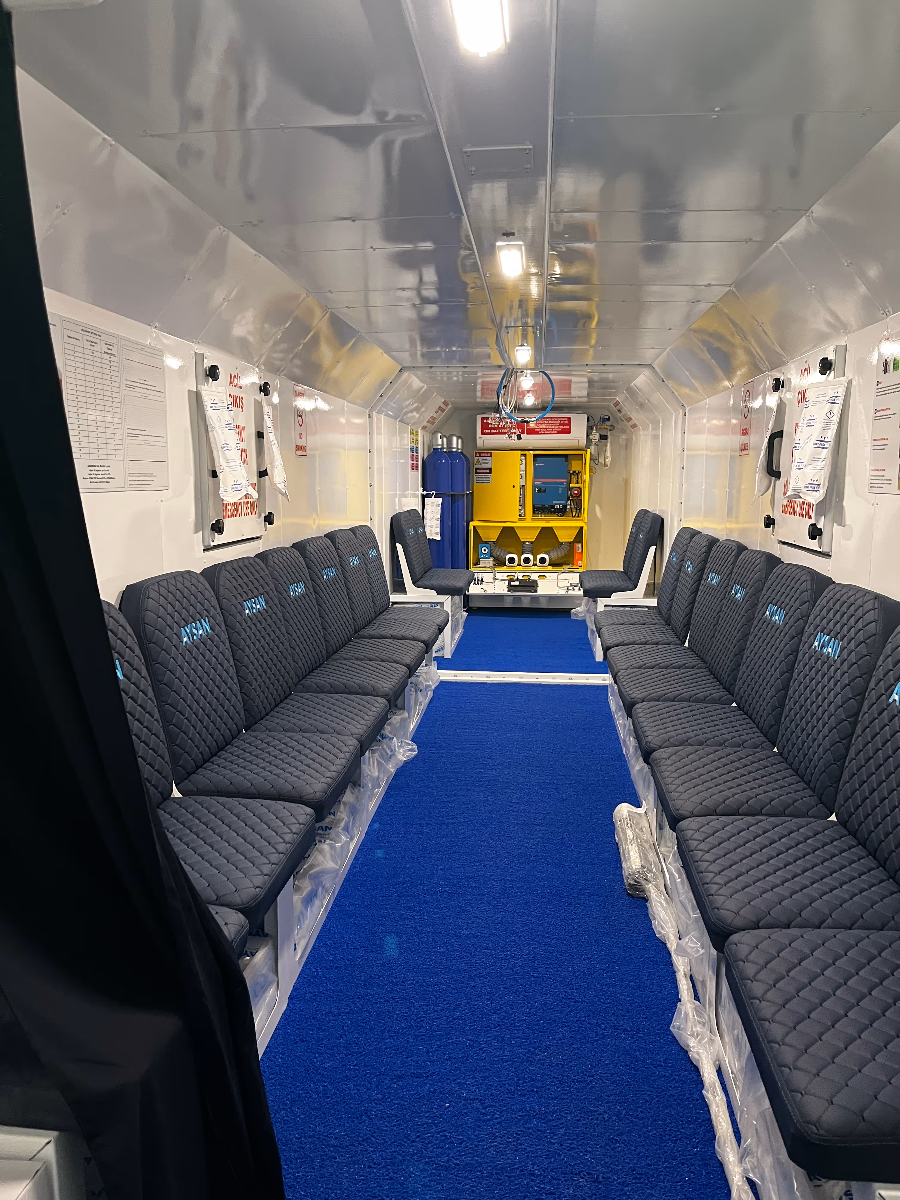 Interior de autobús con asientos negros, alfombra azul y equipamiento de emergencia moderno.