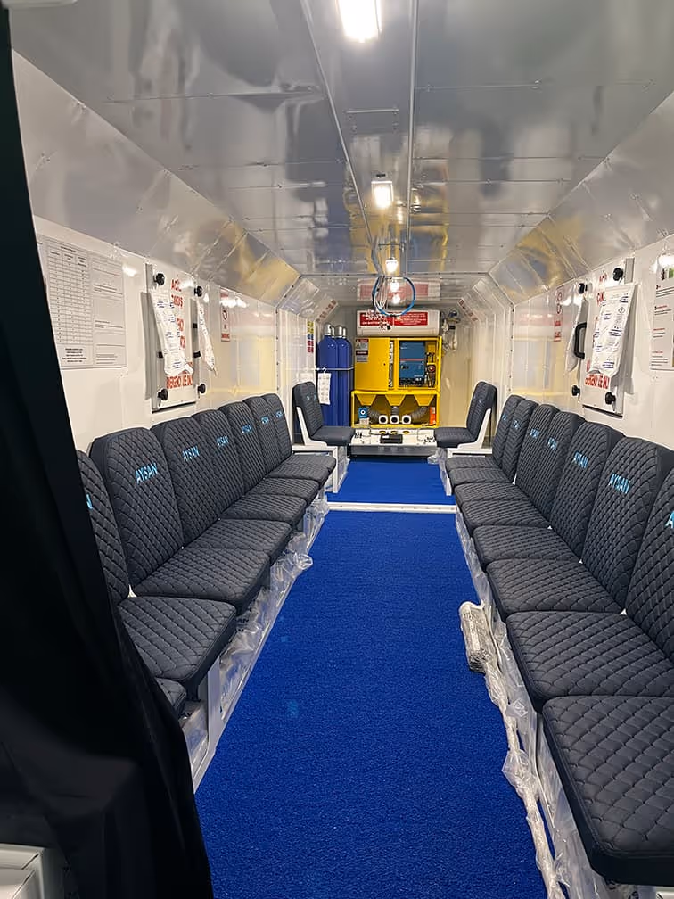 Interior de vagón de tren con asientos negros, pasillo azul y cabina de conducción amarilla
