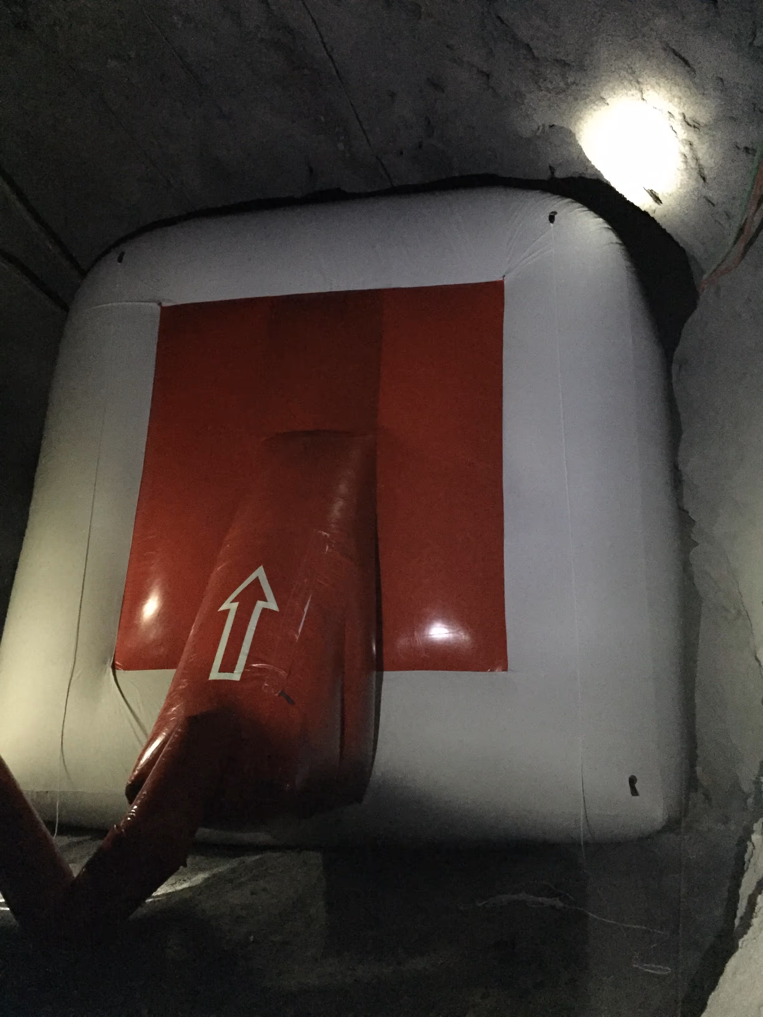 Tubo de respiración rojo con flecha blanca hacia arriba en túnel subterráneo.