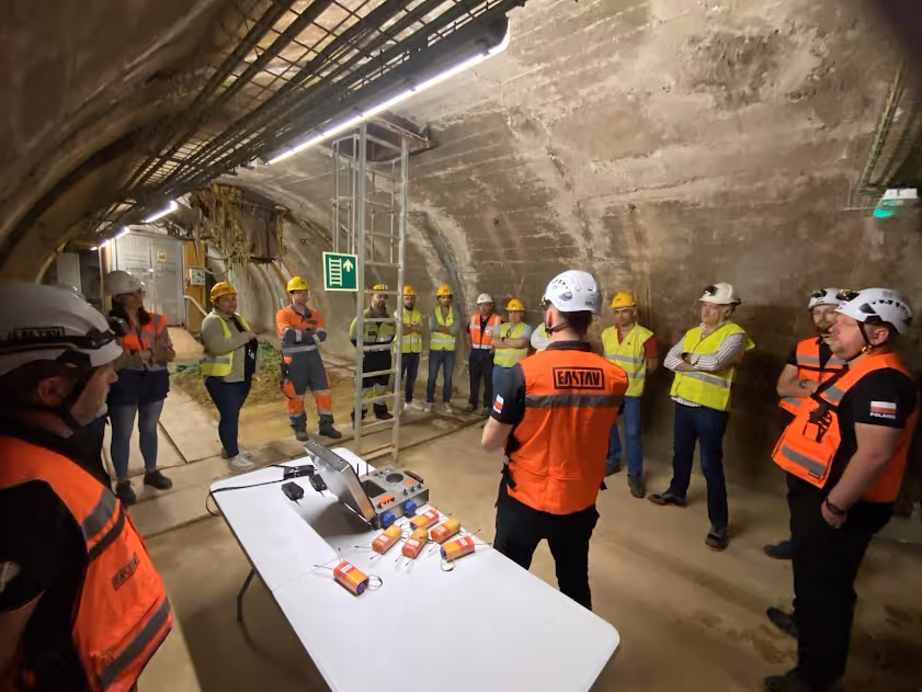 Grupo de trabajadores de construcción con cascos y chalecos reflectantes reunidos en un túnel subterráneo alrededor de una mesa con equipos.