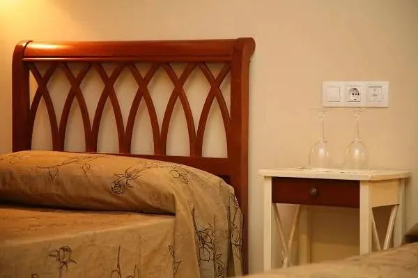 Cabecera de madera con diseño curvo en cama con ropa de cama color beige con estampado floral, junto a una mesa de noche blanca con dos copas colocadas al revés.