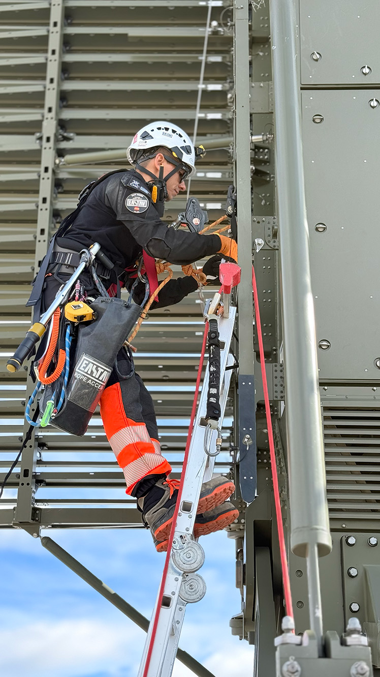 Trabajador con equipo de seguridad subiendo una escalera metálica para mantenimiento industrial.