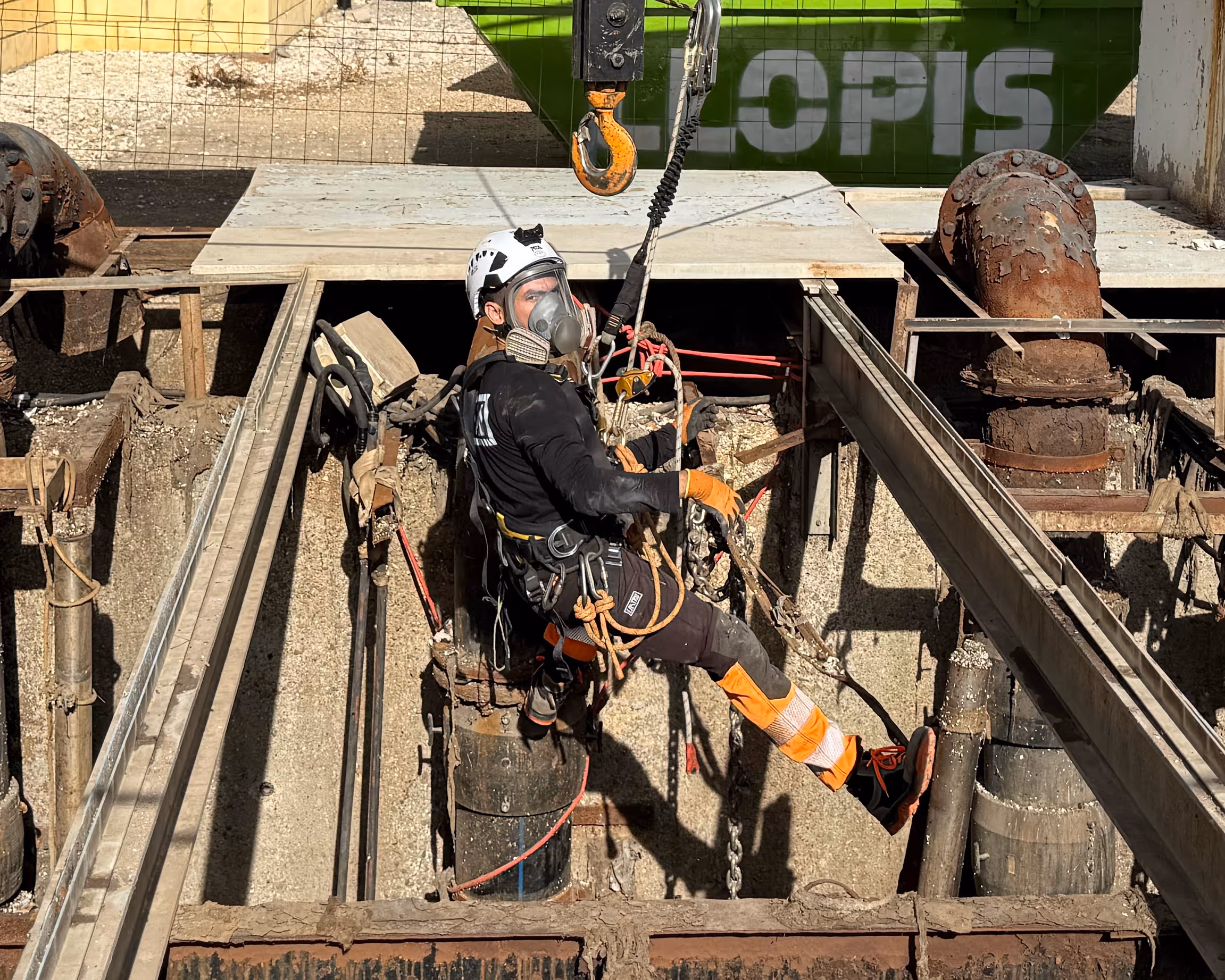 Trabajador con equipo de seguridad y máscara descendiendo en una obra industrial.