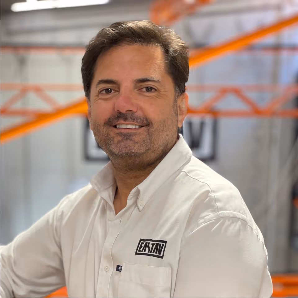 Hombre sonriente en camisa blanca con logotipo en almacén industrial