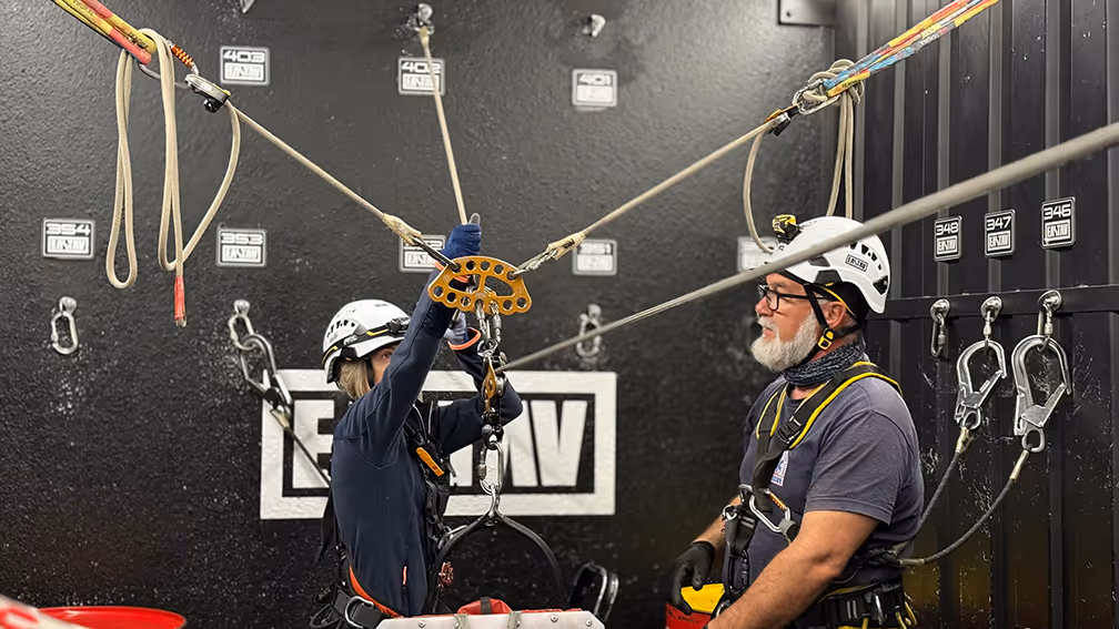 Dos trabajadores en equipo de seguridad inspeccionan equipos de escalada y arneses.