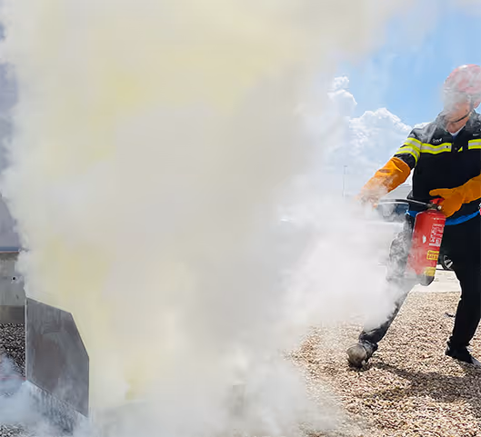 Bombero en equipó de protección usando extintor contra fuego blanco y amarillo.