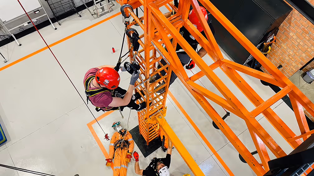 Deportista en casco rojo escalando estructura naranja en competencia de deporte extremo