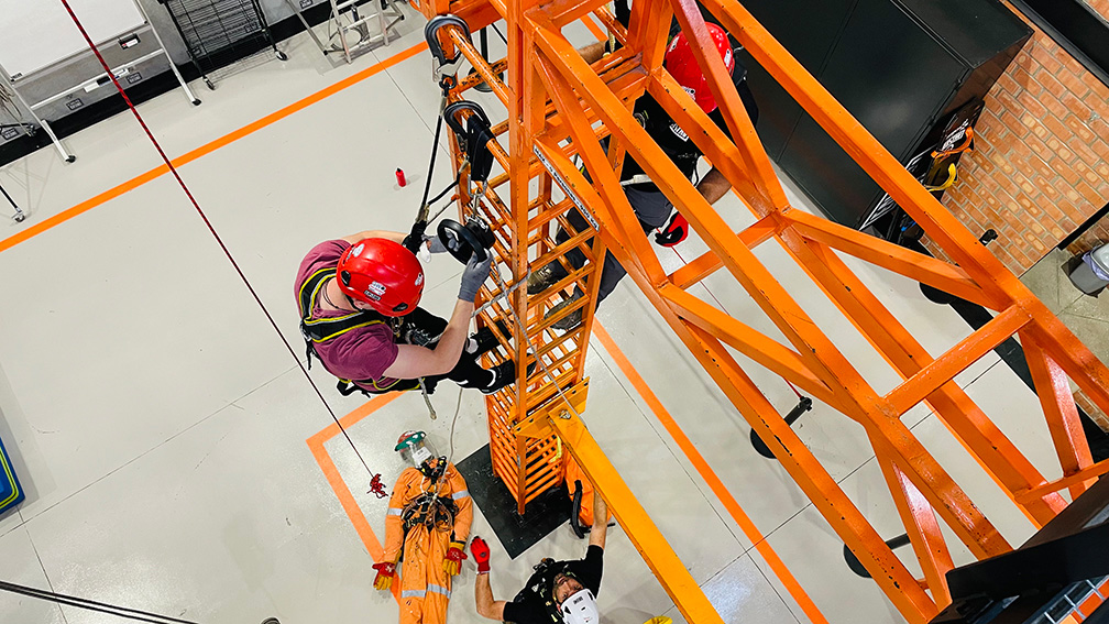 Deportista en casco rojo escalando estructura naranja en competencia de deporte extremo
