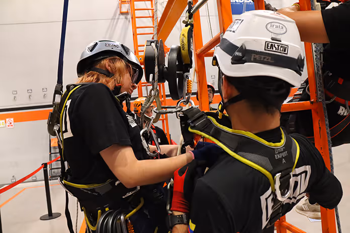 Dos trabajadores con cascos de seguridad operan equipo industrial naranja.