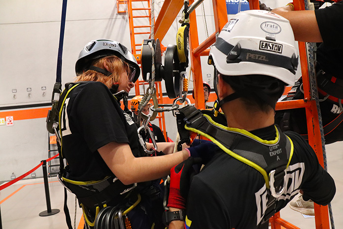 Dos trabajadores con cascos de seguridad operan equipo industrial naranja.