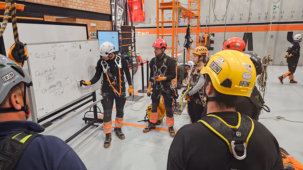 Trabajadores con arneses de seguridad en capacitación dentro de almacén industrial.