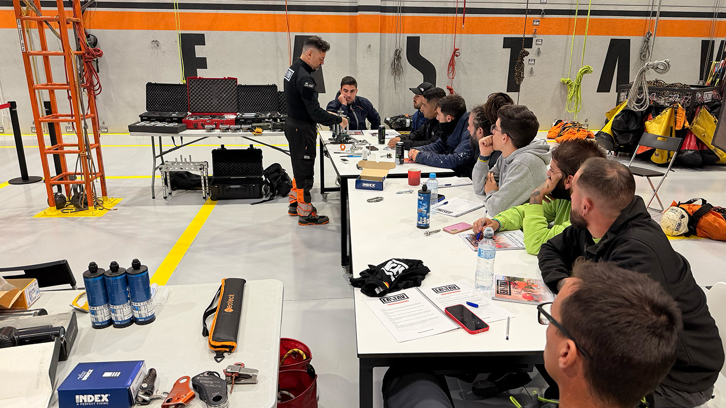 Grupo de trabajadores en capacitación sobre equipos de seguridad en altura en almacén industrial.