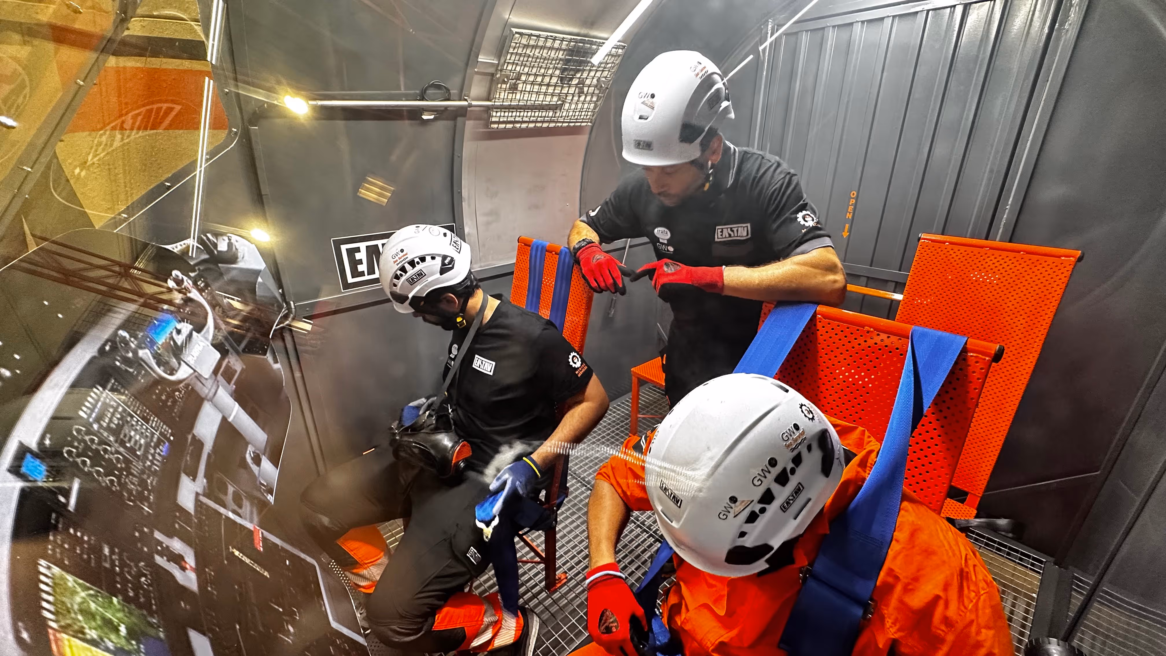 Tres instructores con cascos de seguridad entrenan en una simulación interior, manipulando equipos de rescate aéreo