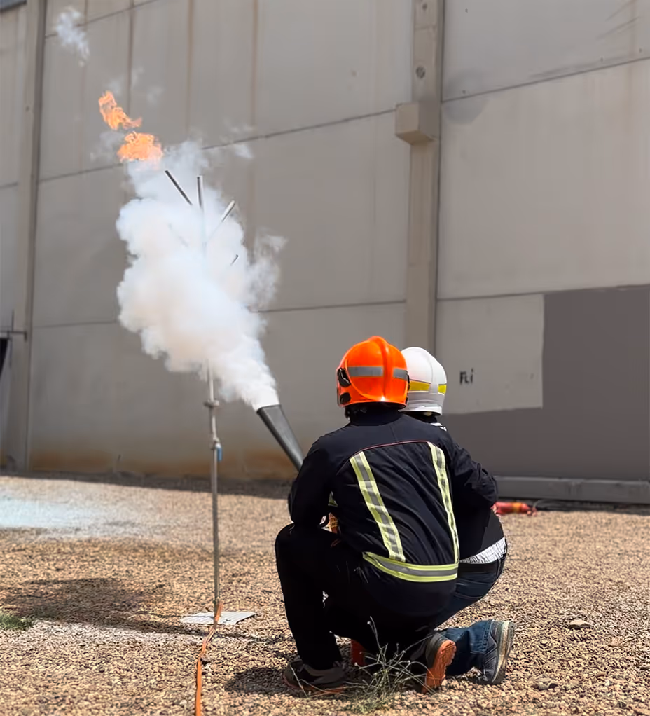 Bombero en equipo protector demostrando extinción de fuego con llamas naranjas.