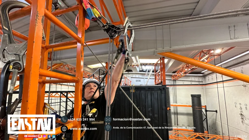 Worker in safety helmet operates lifting equipment in industrial facility with orange machinery