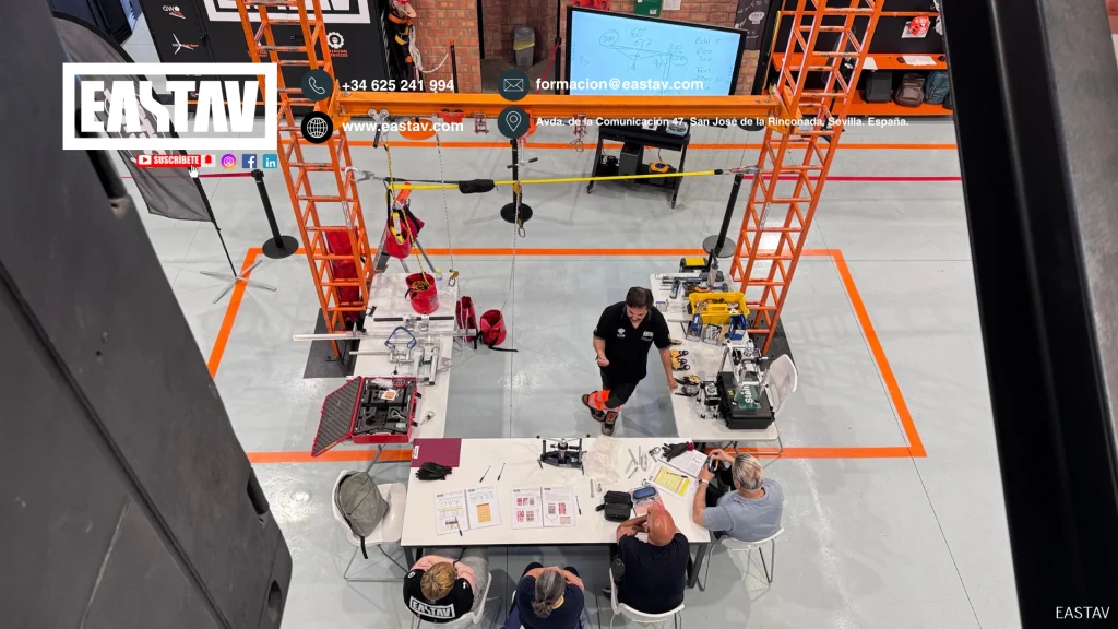 Aerial view of EASTAV workshop with orange scaffolding, workers, robotics equipment, and desk setup.