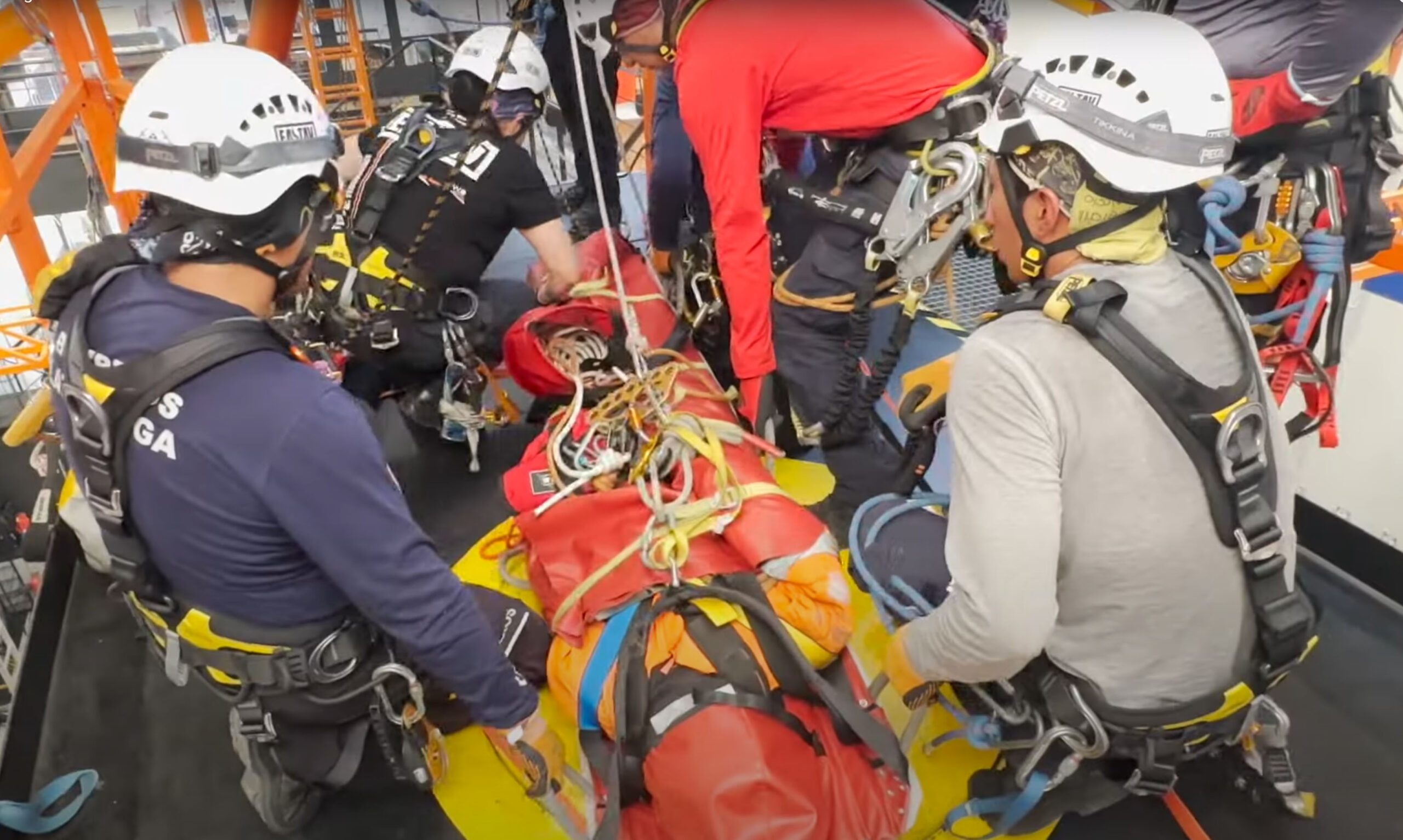 Rock climbers in safety gear practice rescue techniques with ropes and equipment indoors.