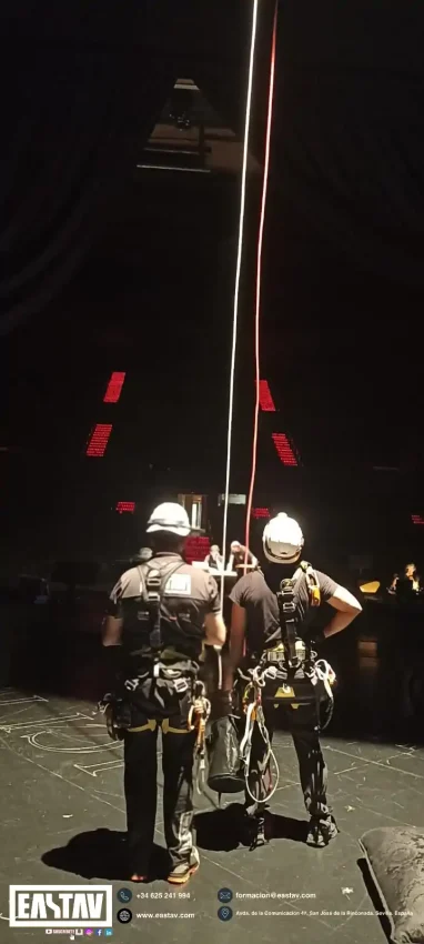 Two construction workers in safety gear climbing vertical ropes during night training exercise