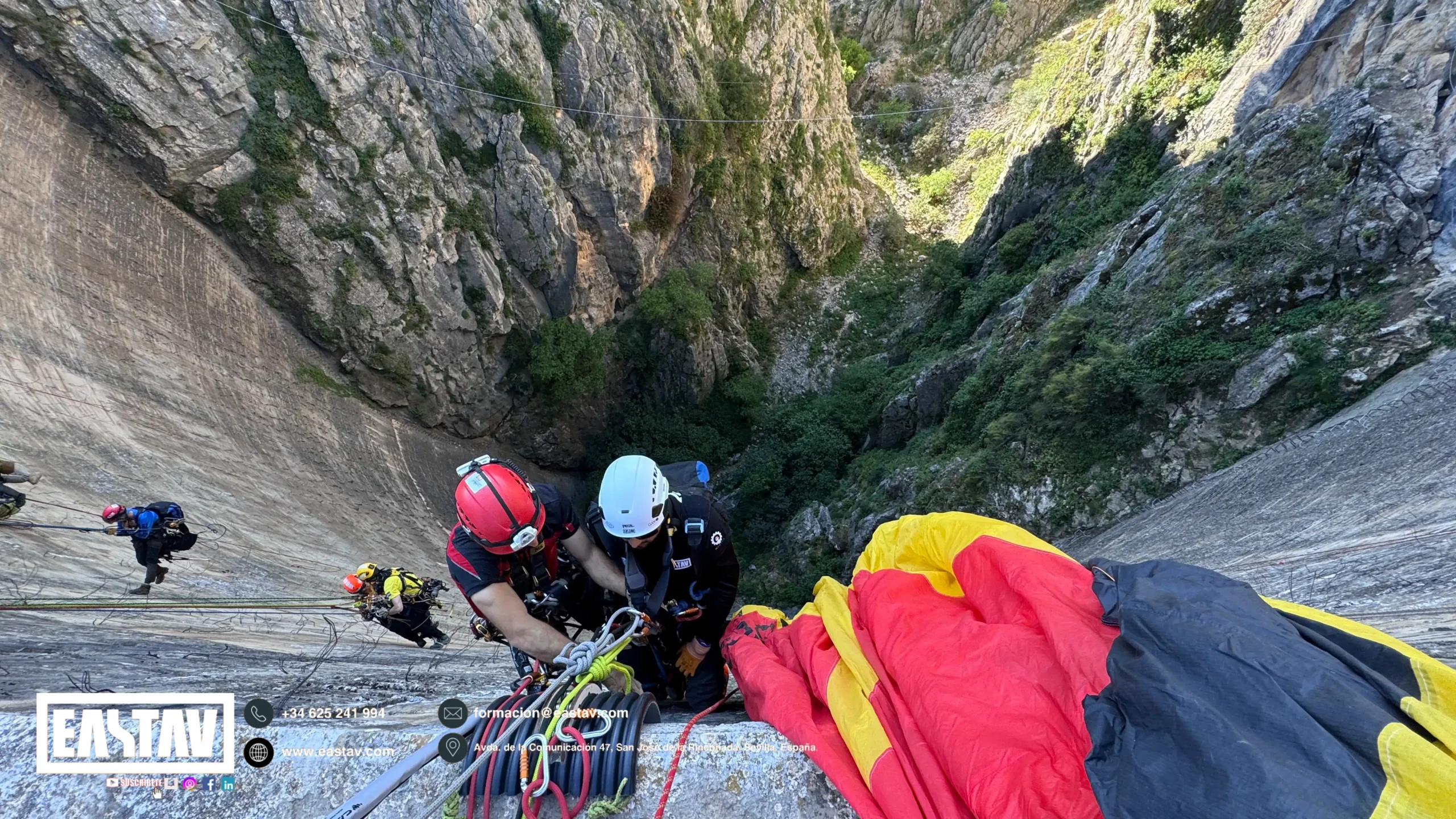 Escaladores en casco rappelando por acantilado rocoso con cuerdas y equipo de seguridad.