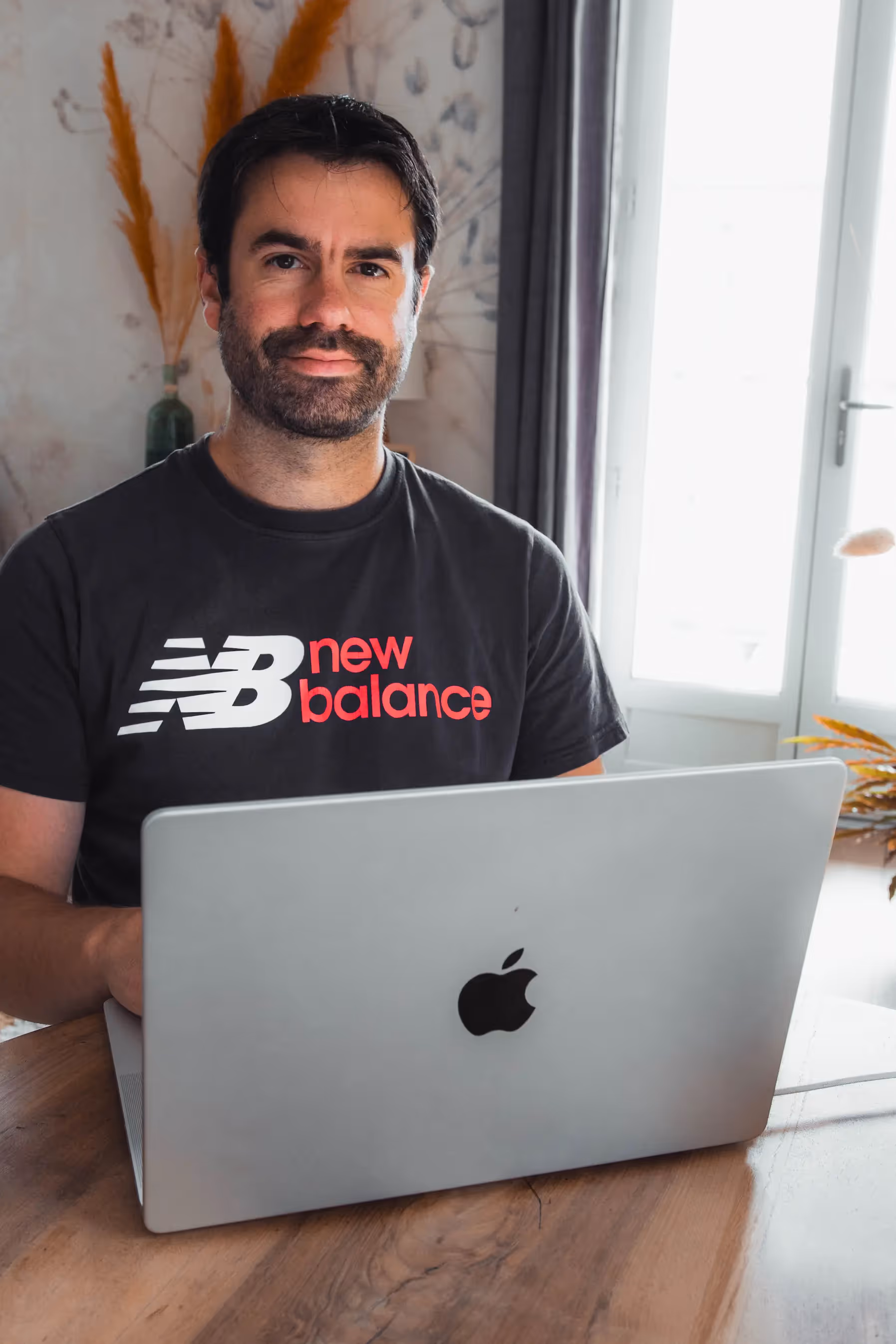 Hombre con camiseta New Balance trabajando en MacBook en escritorio luminoso