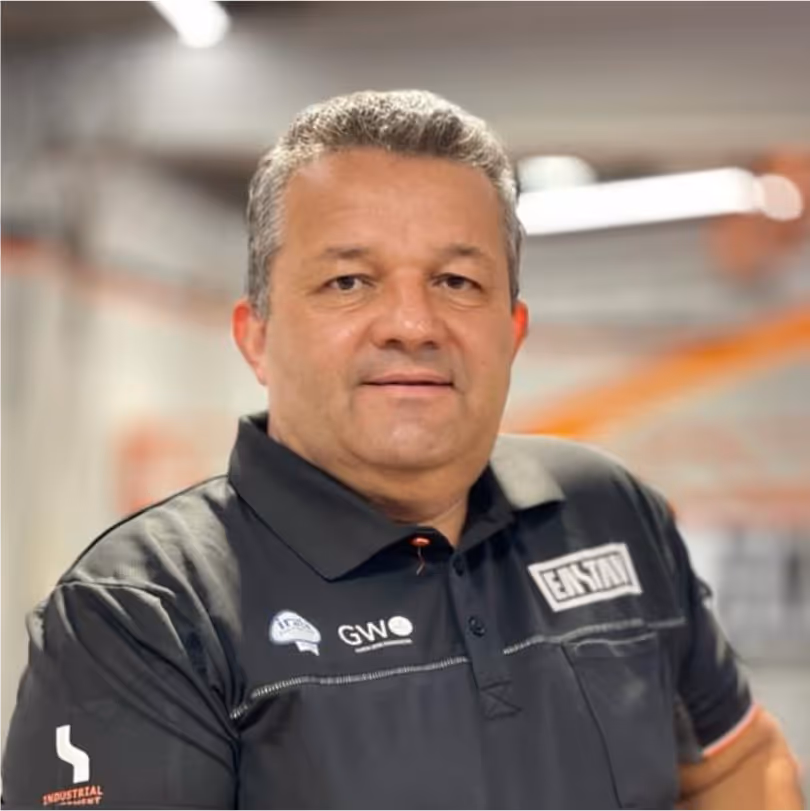 Hombre de mediana edad con cabello gris usa polo negro con logos de empresa.