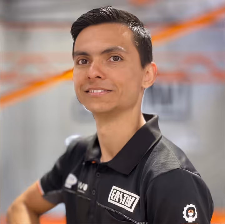 Hombre sonriente con uniforme negro y insignia en fondo borroso de naranja.