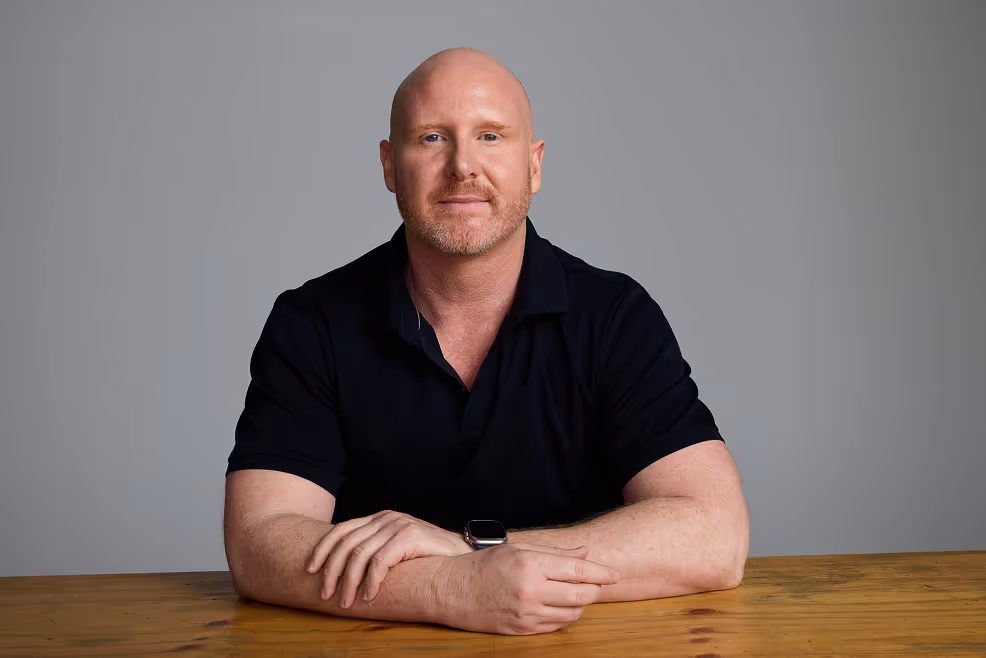 David standing in front of a wooden wall, wearing a dark jacket and looking off to the side