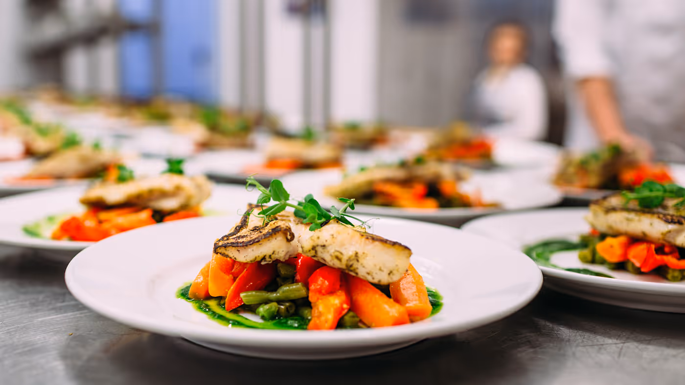 Grillad fisk med grönsaker på elegant tallrik i restaurangköket.