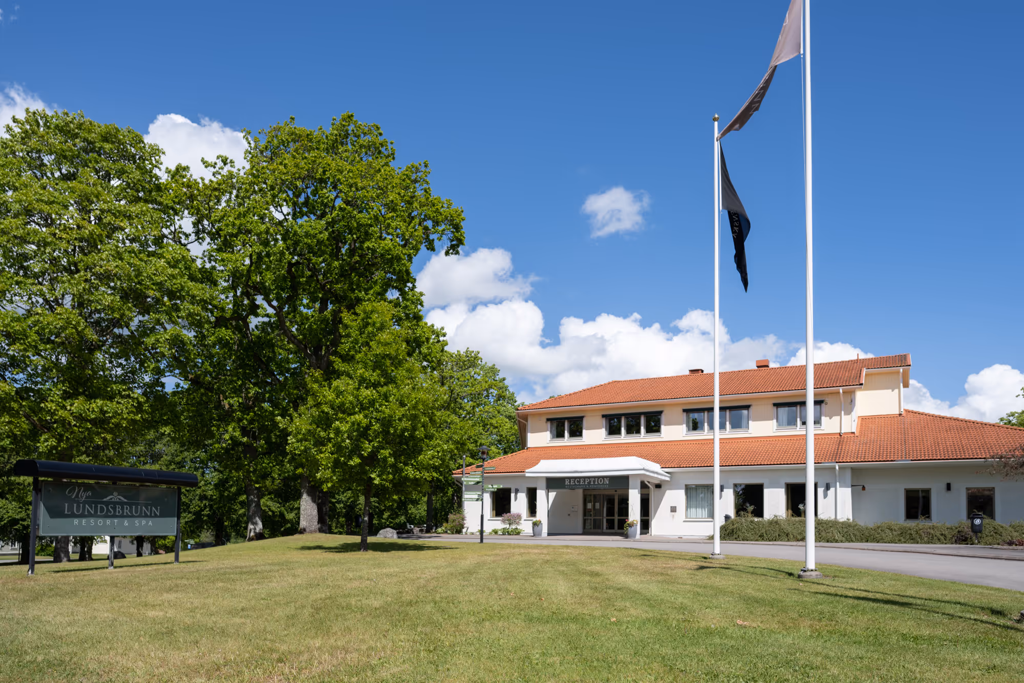 Modern byggnad i grönskande park, soligt väder, blå himmel med moln.