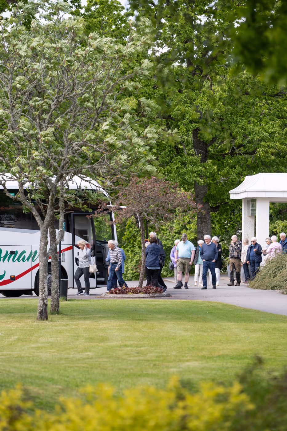 Personer stiger av en turistbuss i en grön trädgård.
