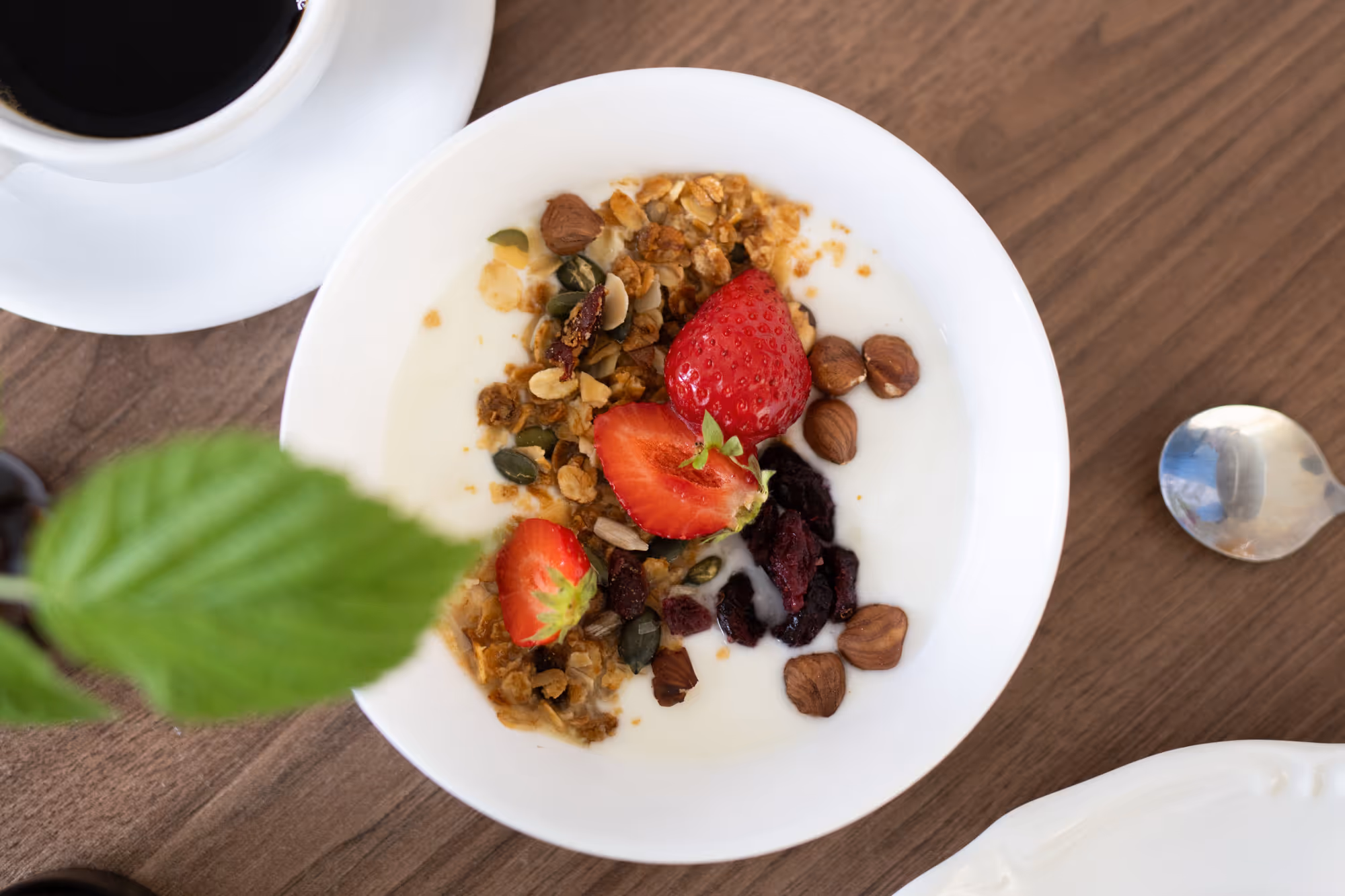 Frukostskål med yoghurt, jordgubbar, nötter och granola på trätallrik.