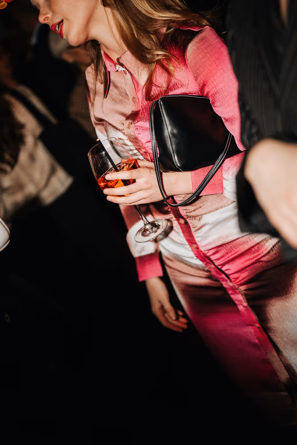 Kvinna i rosa klänning håller ett glas vin på fest.