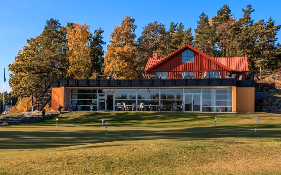 Golfklubbhus i höstlandskap med gröna gräsmattor och träd i bakgrunden.