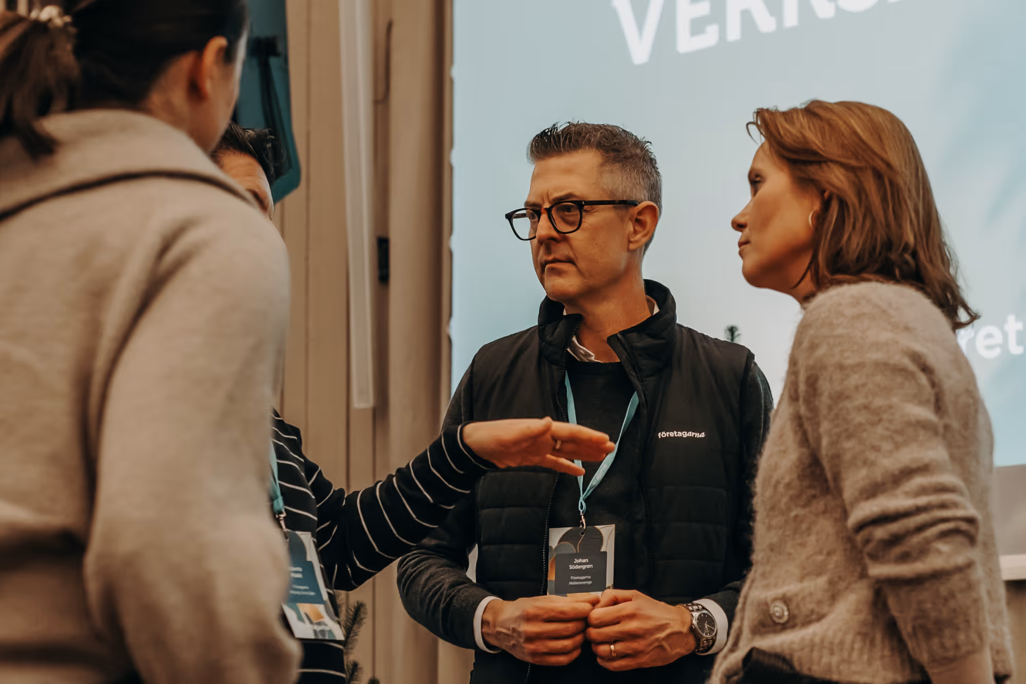 En grupp personer sitter runt ett konferensbord medan en kvinna presenterar och pekar på en whiteboard med diagram och siffror.