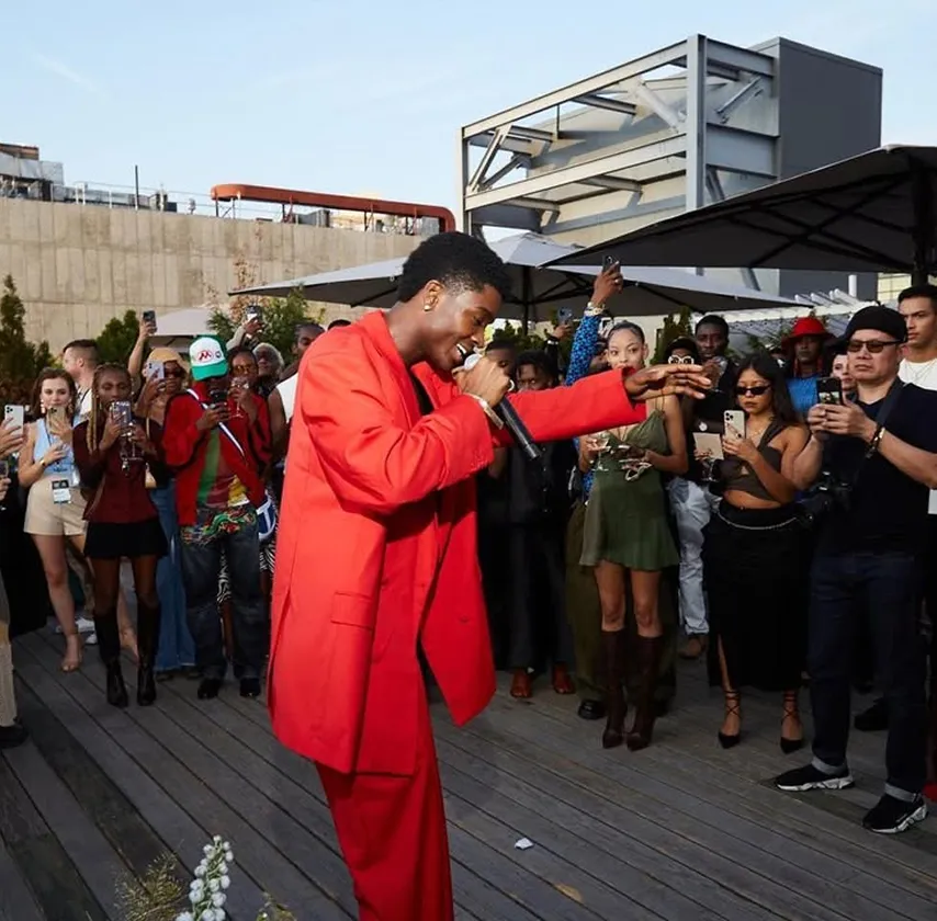 A musician in a bright red suit performs outdoors for a crowd holding up their phones.