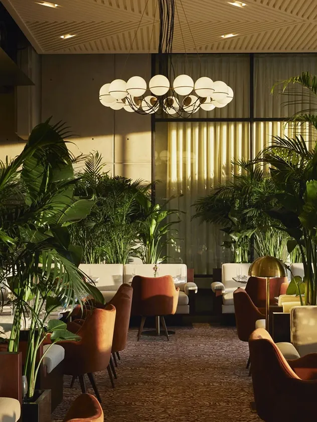 A luxurious hotel lounge or restaurant with lush green plants, modern seating, and globe chandeliers.