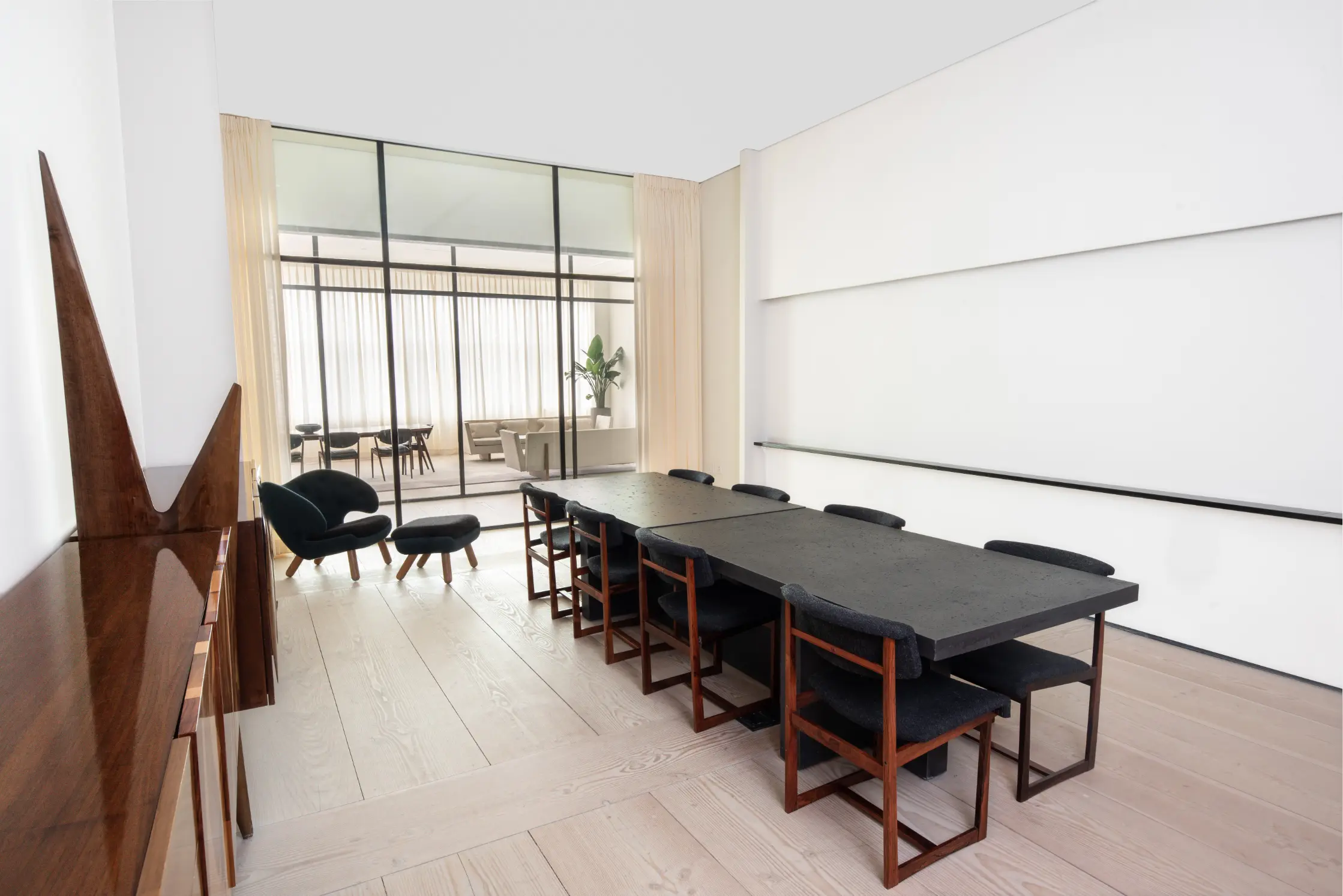 A modern meeting room with a long dark table, chairs, and a large window overlooking a balcony.