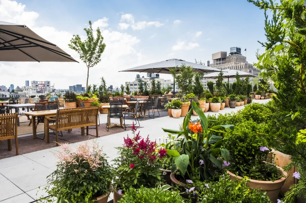 Outdoor terrace at Spring Place featuring dining tables, plants, and skyline view of downtown Manhattan’s One World Trade Center