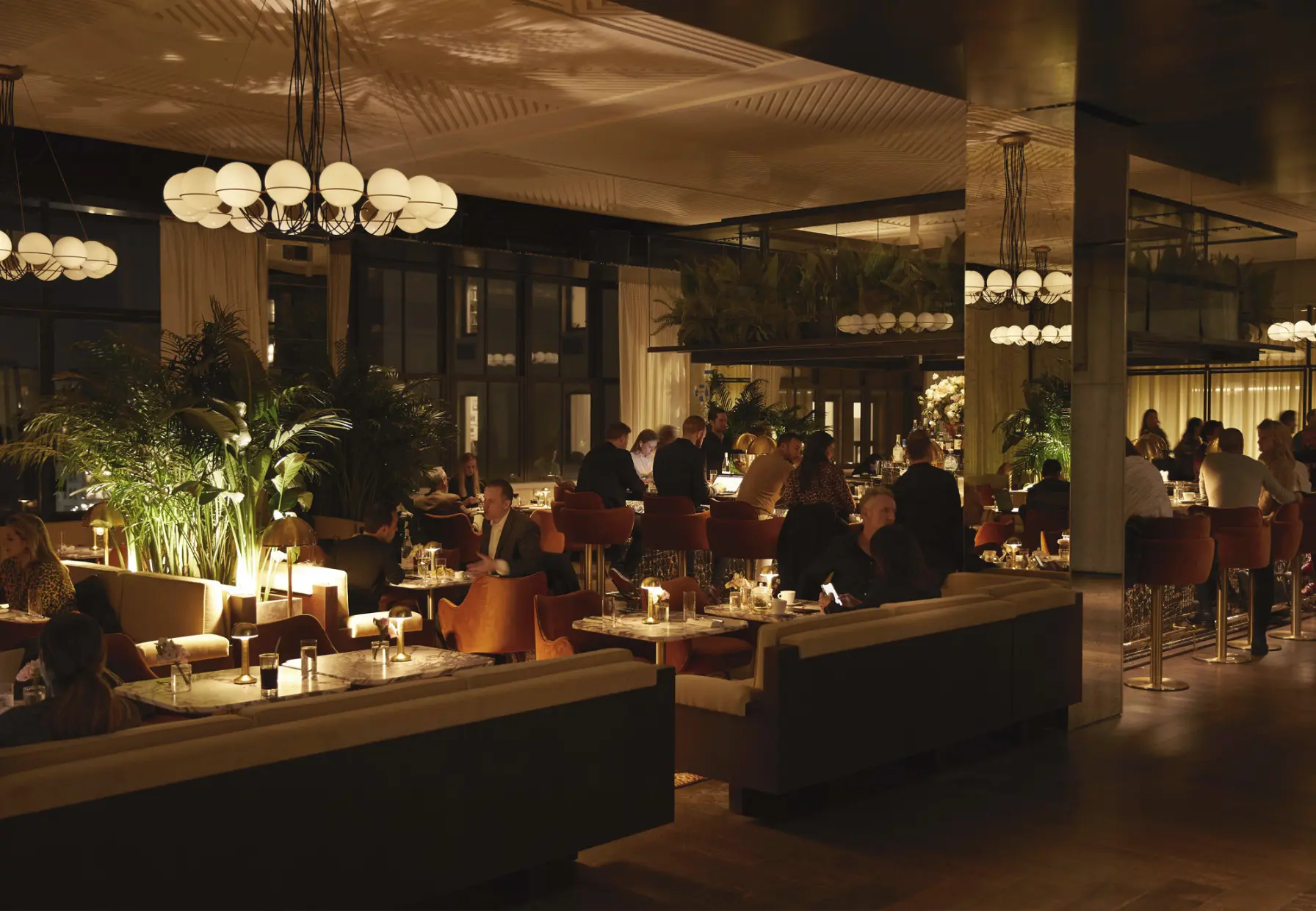 Stylish restaurant at Spring Place with booth seating, lush plants, and globe chandeliers