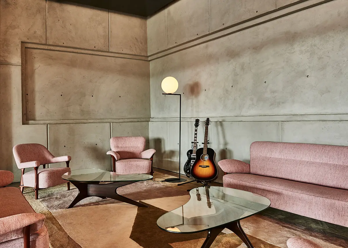 Stylish lounge at Spring Place with pink seating, guitars, and glass tables against concrete walls