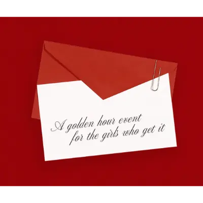 A red envelope with a white card clipped to it, displaying the cursive message: “A golden hour event for the girls who get it” on a deep red background.