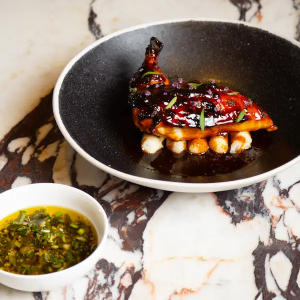 Gourmet roasted quail served over white beans with a side of herb sauce on a marble table - Spring Place