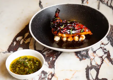 Roasted gourmet quail atop white beans, served with herb sauce on a marble tabletop - Spring Place